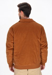 Brun corduroyjakke med krave, ribbede manchetter og kant. Har lodrette striber og en afslappet pasform, der viser en glat tekstur.