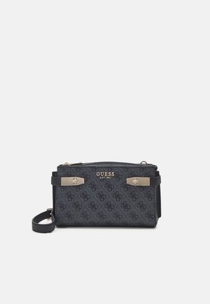 Pochette bracelet noire Guess avec logo doré, surface à motifs, accents métalliques, fermeture éclair et bandoulière amovible sur fond blanc.