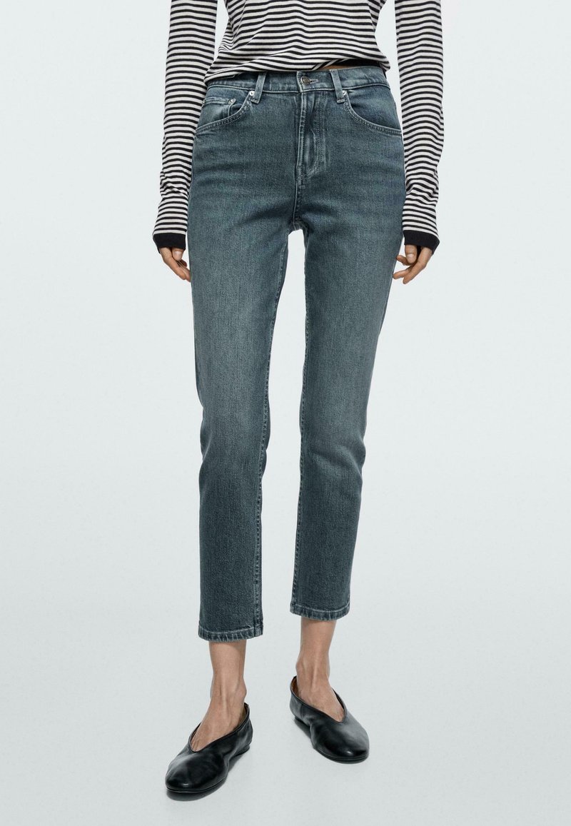 Vrouw draagt korte grijze spijkerbroek, zwarte leren platte schoenen en een zwart-wit gestreept langarmshirt met duimgaten.