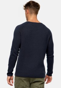Suéter de punto acanalado azul marino de manga larga con hombros raglán, tejido texturizado y diseño ajustado, visto desde atrás.