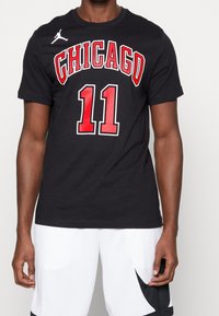 Camiseta de algodón negra con "CHICAGO" en rojo y "11" abajo en rojo con acentos en negro. Logo de Jordan en el hombro izquierdo.