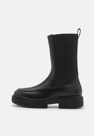 Botte noire mi-mollet avec semelle épaisse à nervures, tige en tissu extensible, bout arrondi et languette à l'arrière.