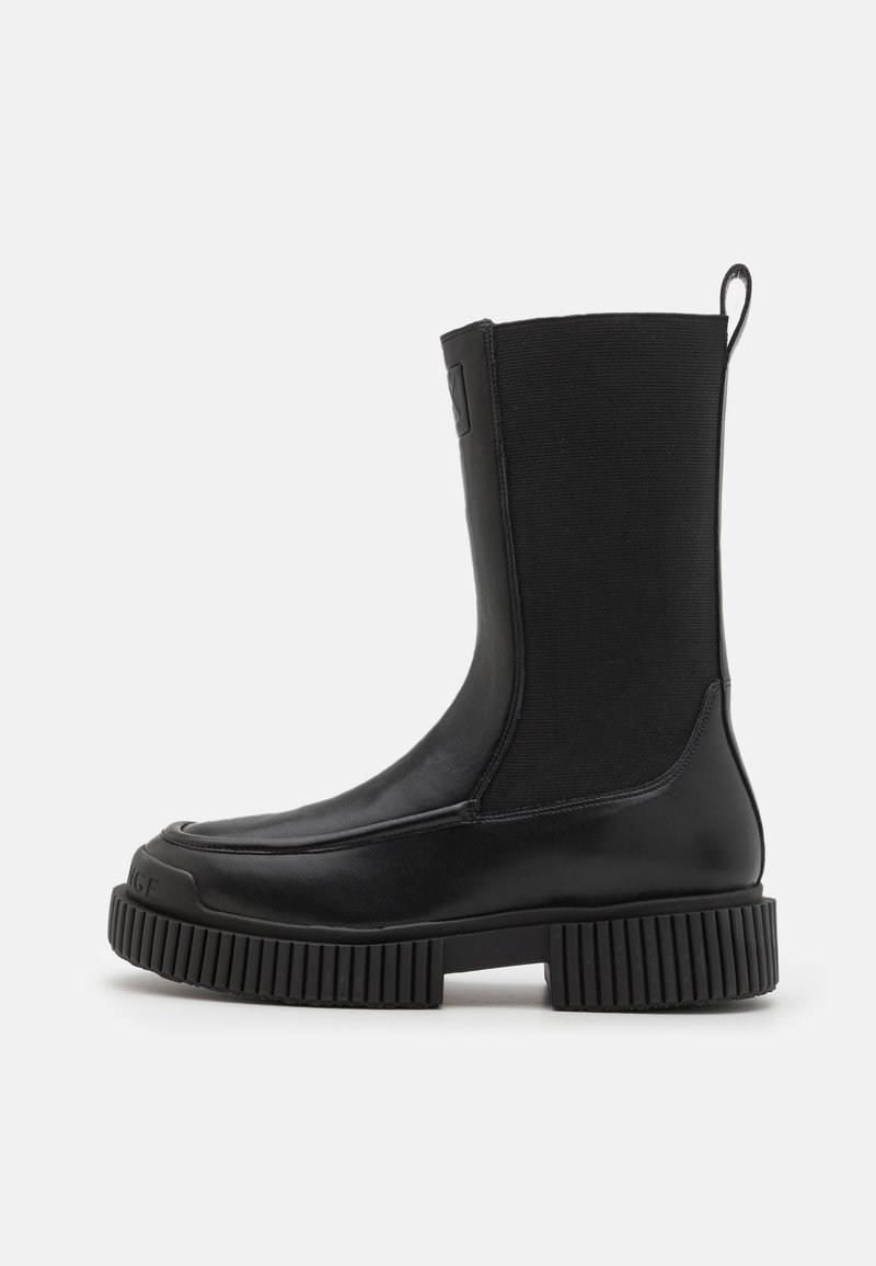 Botte noire mi-mollet avec semelle épaisse à nervures, tige en tissu extensible, bout arrondi et languette à l'arrière.