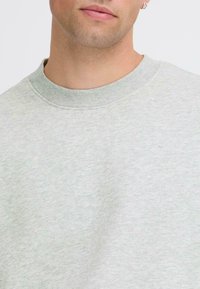 Sweatshirt grigio chiaro a girocollo con finitura texturizzata e colletto a coste. Il tessuto sembra morbido e leggermente patterned.