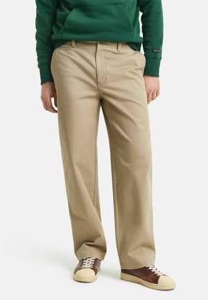Beige chinos with a straight-leg cut. Made of cotton, features side pockets, and classic belt loops. Paired with brown and cream sneakers.