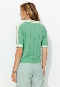 Pull vert à manches courtes avec côtes verticales, accents crème sur le col et les poignets, et un design ajusté. Associé à un pantalon rayé.