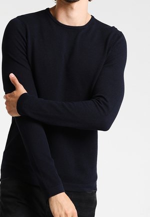 Dunkelblauer Langarm-Strickpullover mit strukturiertem Muster, Rundhalsausschnitt und eng anliegenden Bündchen, kombiniert mit schwarzen Hosen.