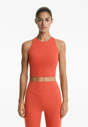 Červený sportovní crop top s vysokým výstřihem, spárovaný s odpovídajícími legínami s vysokým pasem. Hladký, pružný materiál a přiléhavý střih.