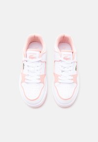 Ζευγάρι λευκά και ροζ αθλητικά παπούτσια Lacoste με κορδόνια, διάτρητο μπροστινό μέρος κα ι το λογότυπο του κροκόδειλου της μάρκας σε κάθε πλευρά.