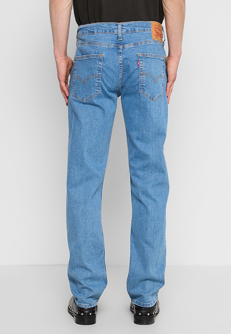 Jeans en denim bleu clair avec une coupe décontractée, des détails de couture visibles et deux poches arrière. Patch logo en cuir sur la ceinture.