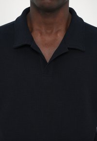 Tricou polo negru, texturat, cu placket butonat și guler moale, având un model strâns și mâneci scurte.