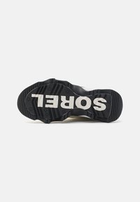 Svart gummisåle til sneakers med markante riller, hvite "SOREL" bokstaver og stjernesymboler; designet egnet for grep og holdbarhet.