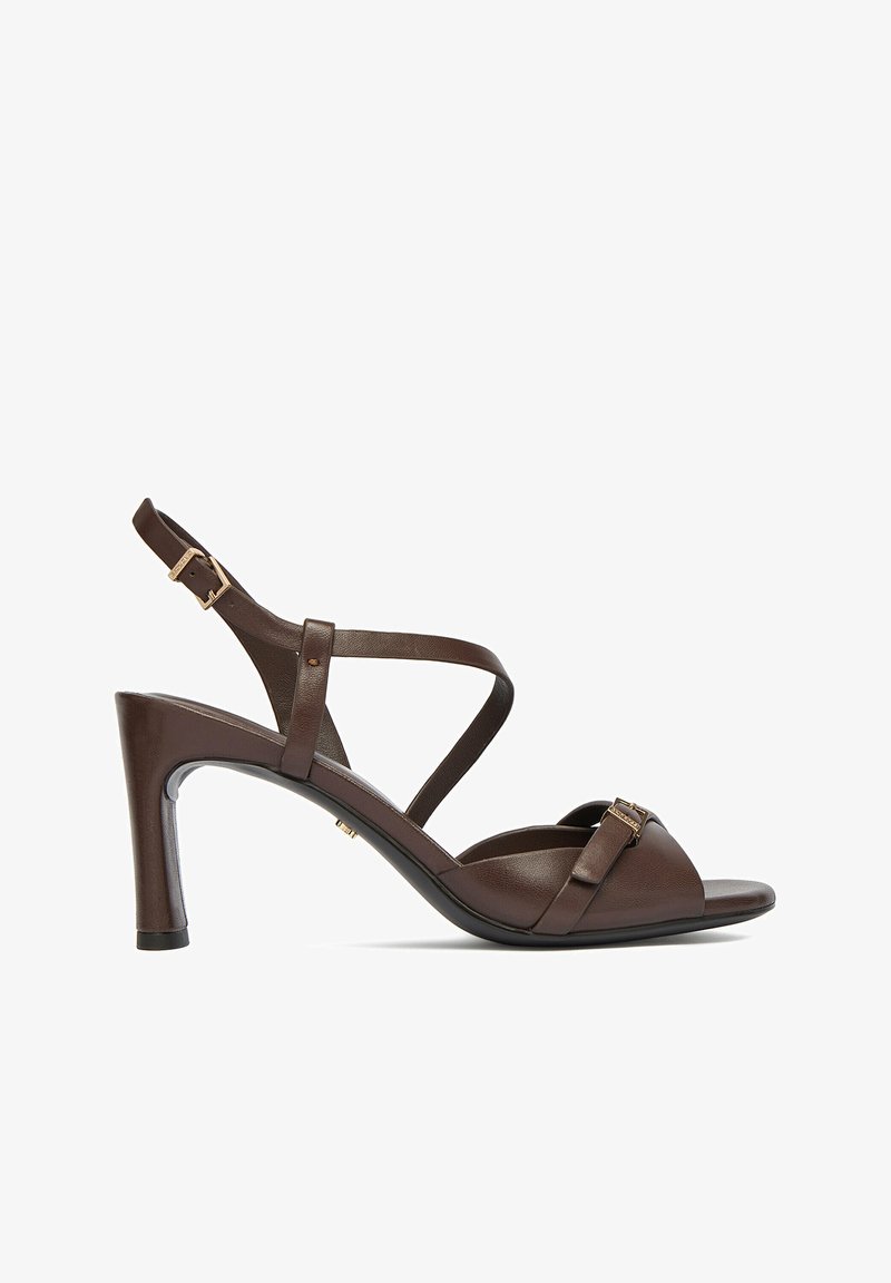 Sandalia de tacón alto de cuero marrón oscuro con correa en el tobillo, cierre de hebilla, punta abierta y tacón delgado sobre fondo blanco.