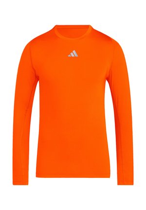 Jasnopomarańczowa, sportowa koszulka z długim rękawem, z okrągłym dekoltem i małym, białym logo Adidas umieszczonym na środku klatki piersiowej.