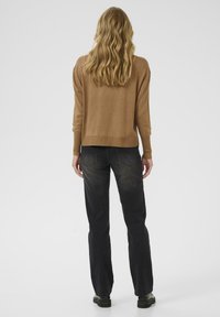 Ljusbrun tröja med långa ärmar, rundad halsringning och ribbad nederkant, i kombination med svarta raka jeans och svarta stövlar.