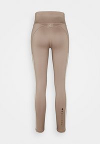 Leggings beige a vita alta con righe laterali, design delle fasi lunari vicino alla caviglia sinistra e dettagli di cuciture curve sul retro.