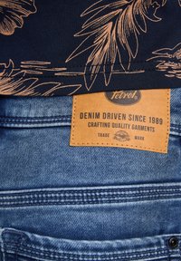 Merihenkinen paita, jossa on ruskehtava kukkakuosi, sinisten farkkujen ylle. Varustettu "Denim Driven Since 1989" -nahkatallella. Tasainen rakenne, rento istuvuus.