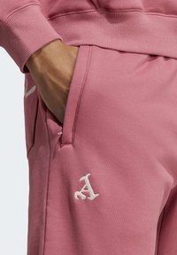 Rosa Sweatshirt mit geripptem Bündchen, ausgestattet mit einem auffälligen weißen gestickten Logo. Die Textur ist weich und lässig, mit einem seitlichen Taschen-Detail.