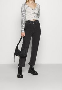 Top corto con un patrón de tie-dye en gris y blanco, combinado con jeans de mezclilla negros de cintura alta y botas negras gruesas hasta el tobillo. Bolso negro.
