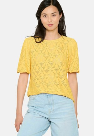 Top giallo a maniche corte con motivo a occhiello scallop, scollatura rotonda e vestibilità ampia, abbinato a jeans azzurri a vita alta.