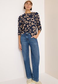 Pullover navy con stampa leopardata beige, girocollo e maniche lunghe; abbinato a jeans a gamba larga blu e scarpe da ginnastica chiare.