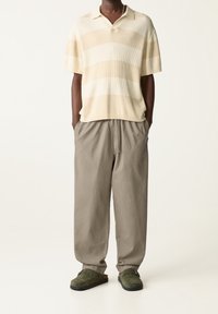 Lichtbeige gebreid poloshirt met horizontale strepen; relaxed-fit grijze broek; groene suède klompen, eenvoudig ontwerp en zachte textuur.