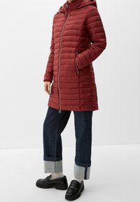 Rode gewatteerde jas met horizontaal quiltpatroon, ritssluiting aan de voorkant, capuchon en zijzakken. Gecombineerd met donkere spijkerbroeken en zwarte instappers.