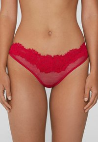 String en dentelle rouge avec motif floral �à la taille, doté d'un corps en résille et d'une texture douce. Coutures plates et absence de ferrures visibles.