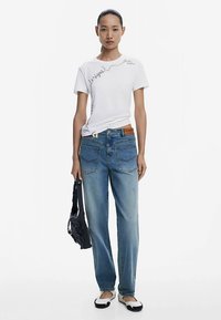 Vit tajt t-shirt med svart grafik, blå löst sittande jeans, svart väska och svarta och vita platta skor. Sidenmjuk tyg och denimstruktur.