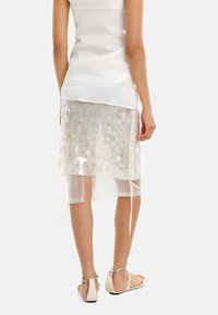 Biała półprzezroczysta asymetryczna spódnica z detalami z cekinów, warstwowym designem i akcentami ze sznurkiem. W połączeniu z minimalistycznymi sandałami.