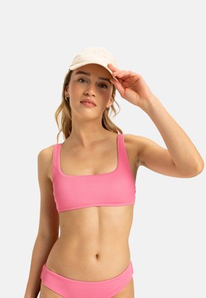 Pink ribbed bikini top with square neckline, wide straps, and coordinating bottoms. Model wearing a beige cap, with natural hair texture visible.