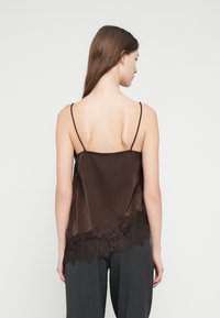 Brun silke-kamisol med tynne stropper, med dekorativt blonderkant. Jevn tekstur, løs passform og subtil glans. Enkelt bakgrunn.