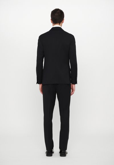 Traje negro con un corte ajustado, que presenta una chaqueta de un solo botón y pantalones estrechos, confeccionado en una tela suave, mostrado desde la parte posterior.