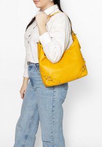 Gele leren tas met een zachte textuur en zilveren hardwareaccenten. Met een slungelige vorm en een verstelbare schouderband.