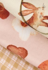 Tre lag stof: øverst med mønster af kaniner og blade på cremefarvet baggrund, midt med lyserøde hjerter og blomster, nederst med gyldent ternet mønster.