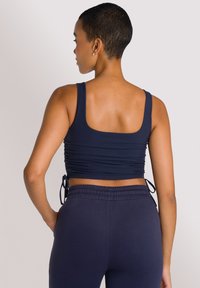 Top corto a costine blu navy con lacci laterali regolabili, abbinato a pantaloni a vita alta blu navy scuri, caratterizzati da una texture liscia e un design aderente.