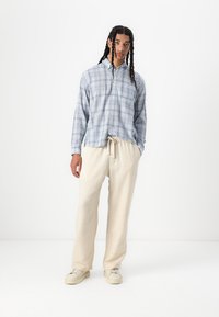 Blue and white plaid button-up shirt with long sleeves, paired with light beige drawstring pants and cream sneakers. Smooth fabric texture.