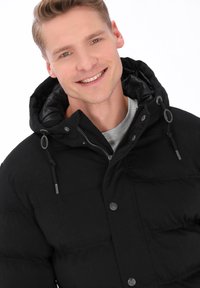 Czarna kurtka puchowa z pikowanym wzorem, regulowanym kapturem i szarą wyściółką na zamek. Posiada zatrzaski i ozdobne sznurki.