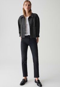 Giacca nera strutturata con chiusura a bottone, abbinata a una maglietta bianca e jeans neri slim-fit. Mocassini neri completano l'outfit.