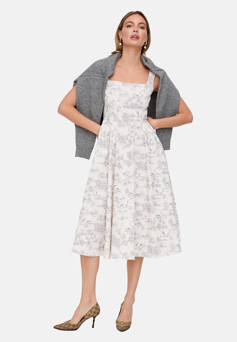 Weißes Kleid mit Blumenmuster, quadratischem Ausschnitt und ausgestelltem Rock; kombiniert mit einer grauen Strickjacke und braunen, gemusterten High Heels.