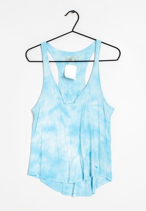 Camiseta sin mangas con espalda racer y efecto tie-dye azul claro, con etiqueta colgando de una percha negra sobre fondo blanco.