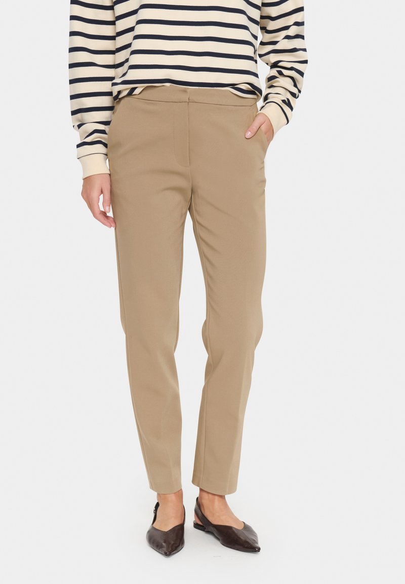 Pantalons fuselés beiges avec une texture lisse, dotés de poches latérales et d'un design à l'avant plat. Associés à une chemise rayée à manches longues.