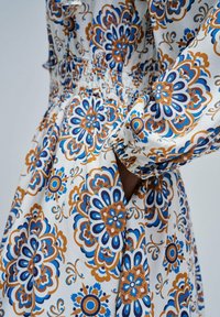 Vestido con estampado floral que presenta diseños en azul y naranja sobre una tela blanca. La cintura elástica y las mangas fruncidas aportan estructura y detalle.