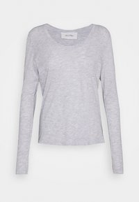 Gaiši pelēka garroku T-krekls, izgatavots no mīksta, plāna auduma. Ir apaļš kakla izgriezums un vaļīgs piegriezums ar šūtiem apmalēm.