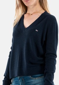 Maglione blu navy a scollo a V realizzato in tessuto morbido, con polsini e orlo a costine, caratterizzato da un piccolo logo sulla parte sinistra del petto.