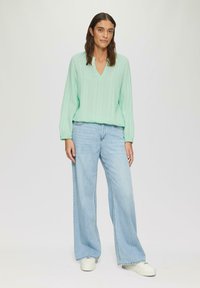 Blouse verte menthe à manches longues avec un col en V et une finition texturée, associée à un jean bleu clair à jambe large et des baskets blanches.