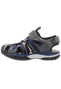 Sandal gris y azul marino hecho de materiales sintéticos, con diseño de punta abierta, correa ajustable y acentos con patrón para ventilación.