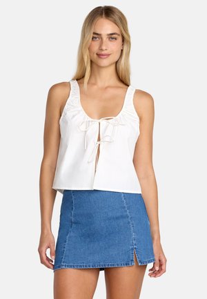 Weißes, bauchfreies Oberteil mit vorderer Bindung und gerafften Trägern, kombiniert mit einem blauen Jeans-Minirock mit seitlichem Schlitz.