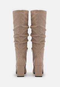Knähöga beige stövlar i slätt material med en slouch-design, fyrkantiga klackar och blixtlås på sidan för enkel påklädnad.