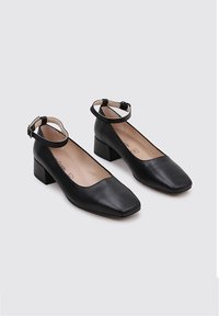 Chaussures noires en cuir à talon carré avec un bout carré et une bride de cheville. Texture lisse et design minimaliste, avec une doublure beige.